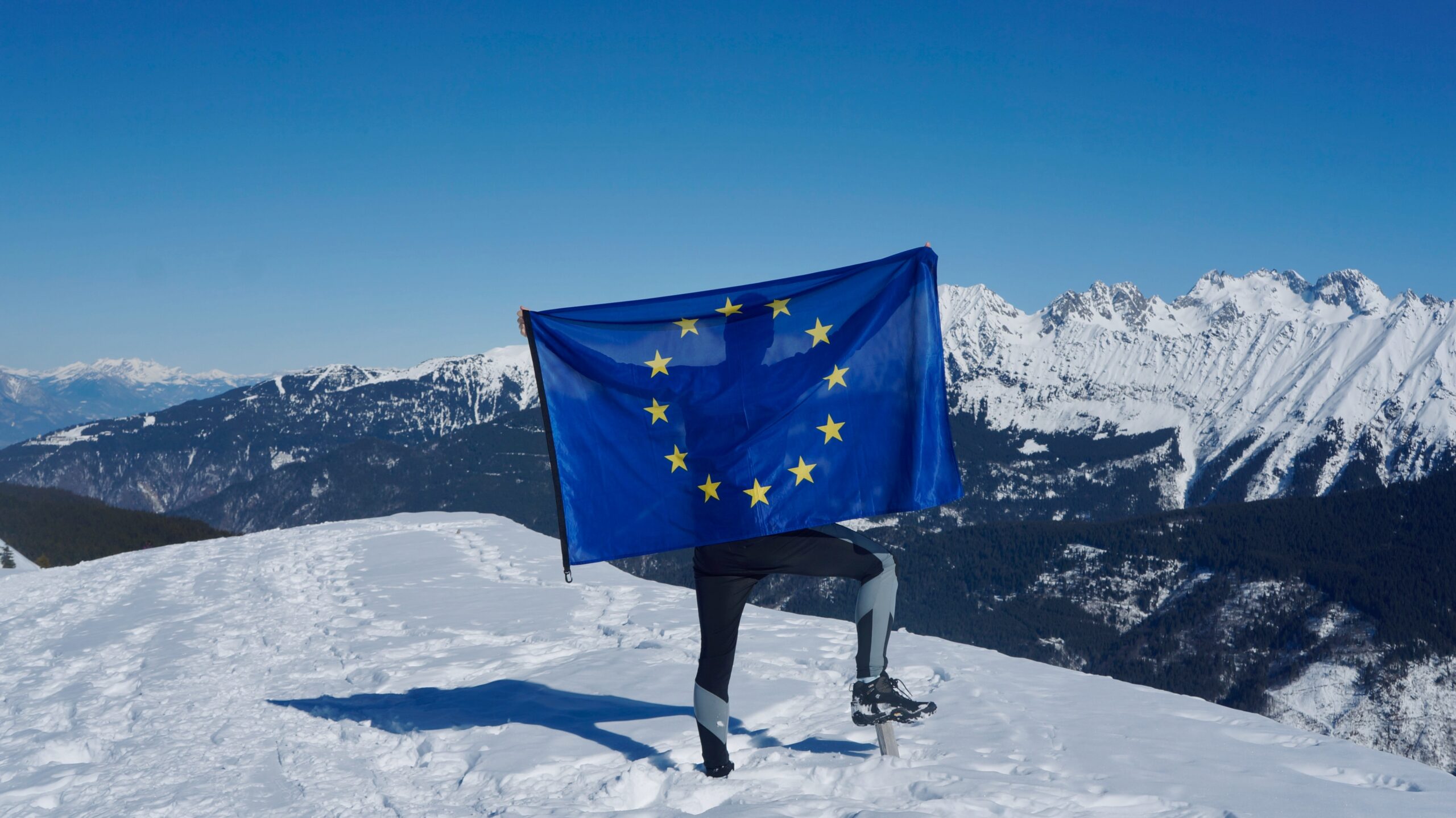 man holding up european flag on snowy mountains