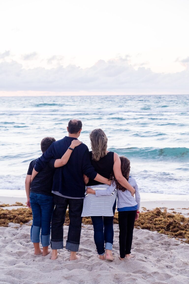 family hugging on the sand looking out to the sea
