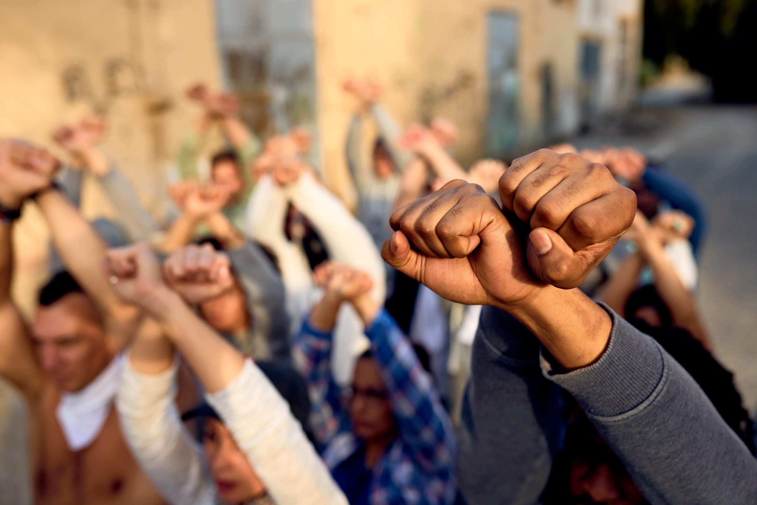 Close-up Of Large Group Of Protesters With Clenched Fists Above heads