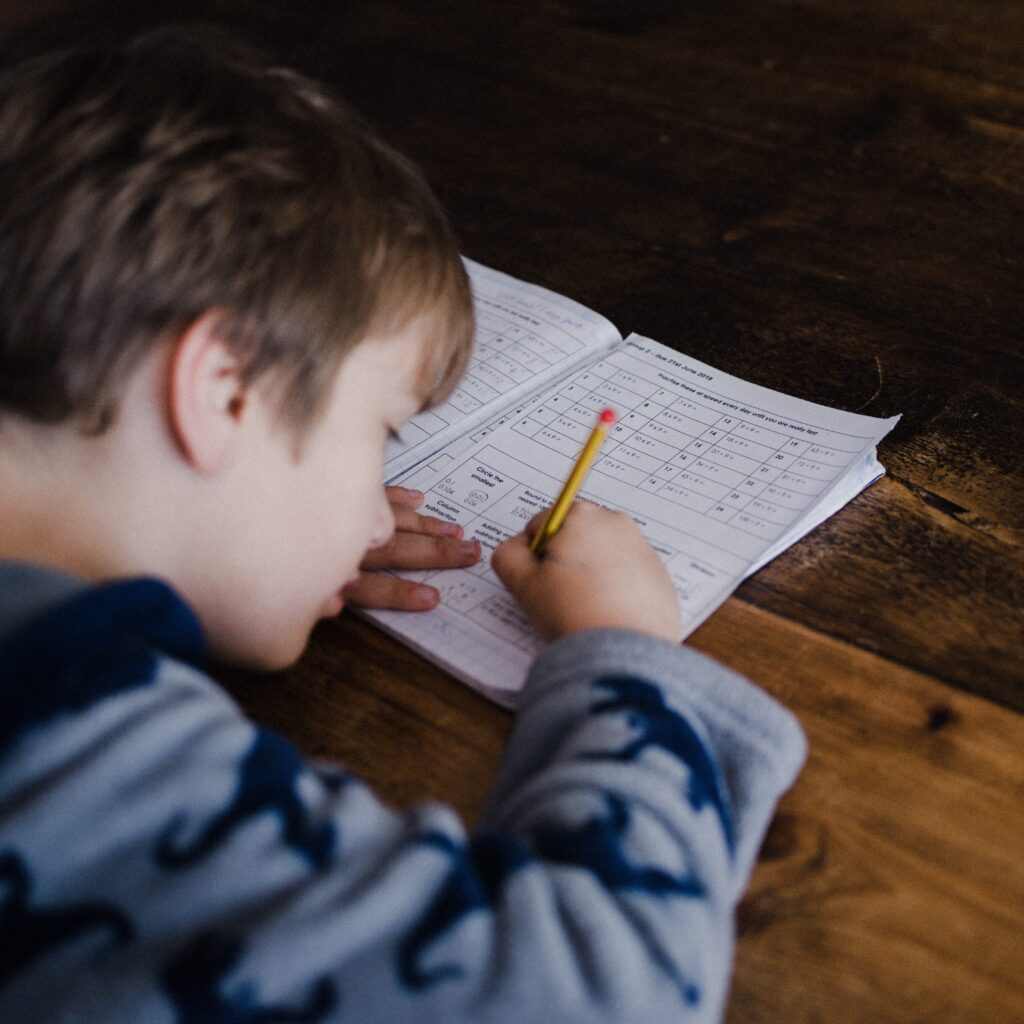 young boy writing in book with pencil